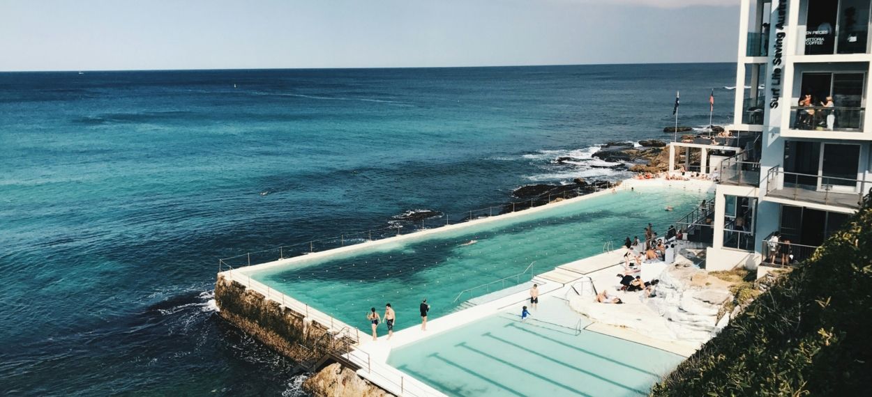 Two pools by the ocean with people swimming and a surf lifesaving club, Photo by caroline voelker on Unsplash