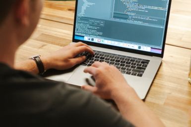 Software developer working on a laptop displaying code, sitting at a table