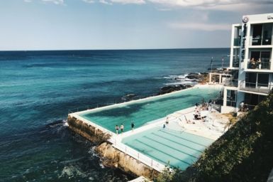 Two pools by the ocean with people swimming and a surf lifesaving club, Photo by caroline voelker on Unsplash