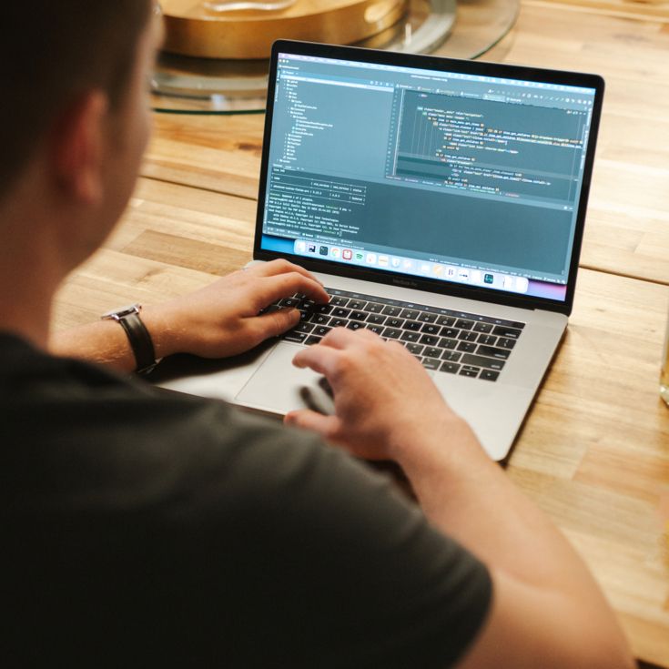 Software developer working on a laptop displaying code, sitting at a table