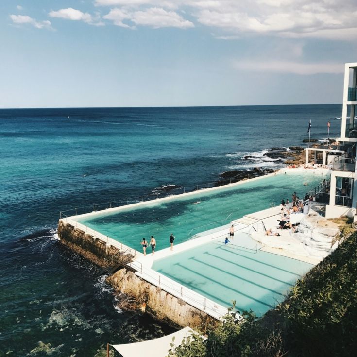 Two pools by the ocean with people swimming and a surf lifesaving club, Photo by caroline voelker on Unsplash