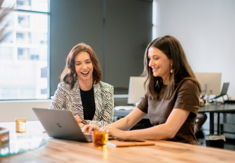 Two women in an office collaborating on a project while working on a laptop